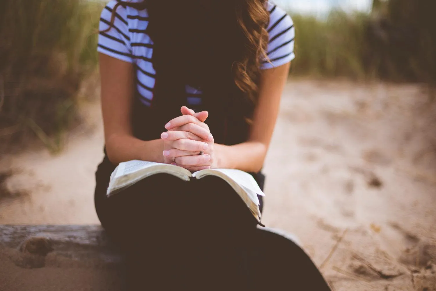 Open hands in prayer resting on an open Bible before study time